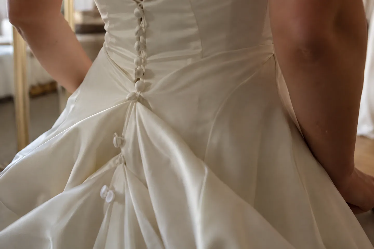 Hand-stitched bustle loops and buttons on the back of a satin wedding gown