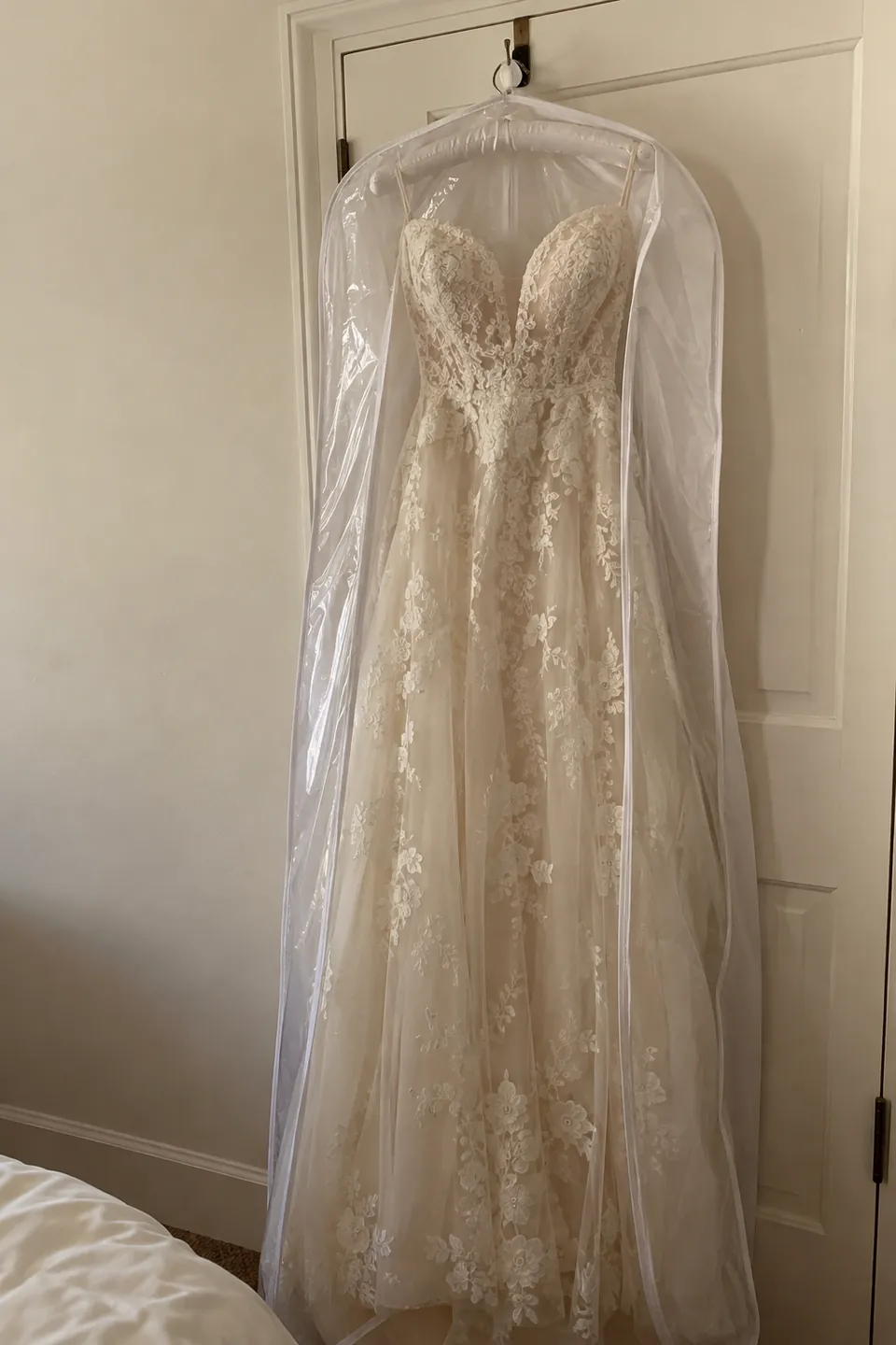 A wedding gown on a padded hanger inside a garment bag, hung from a door