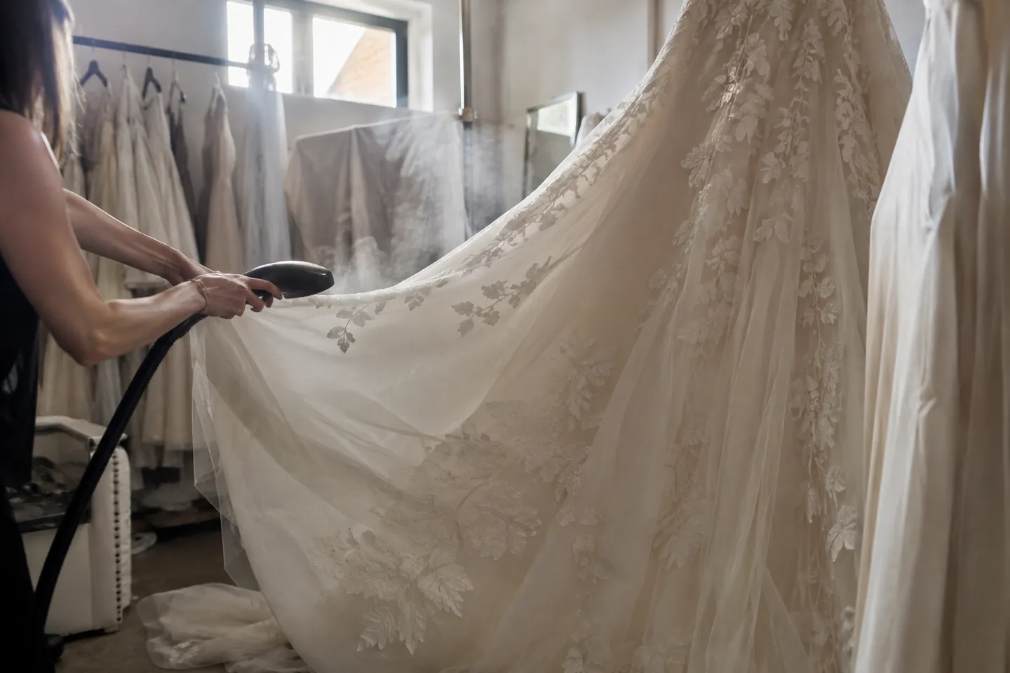 A wedding gown's skirt being steamed in a back room, steam rising