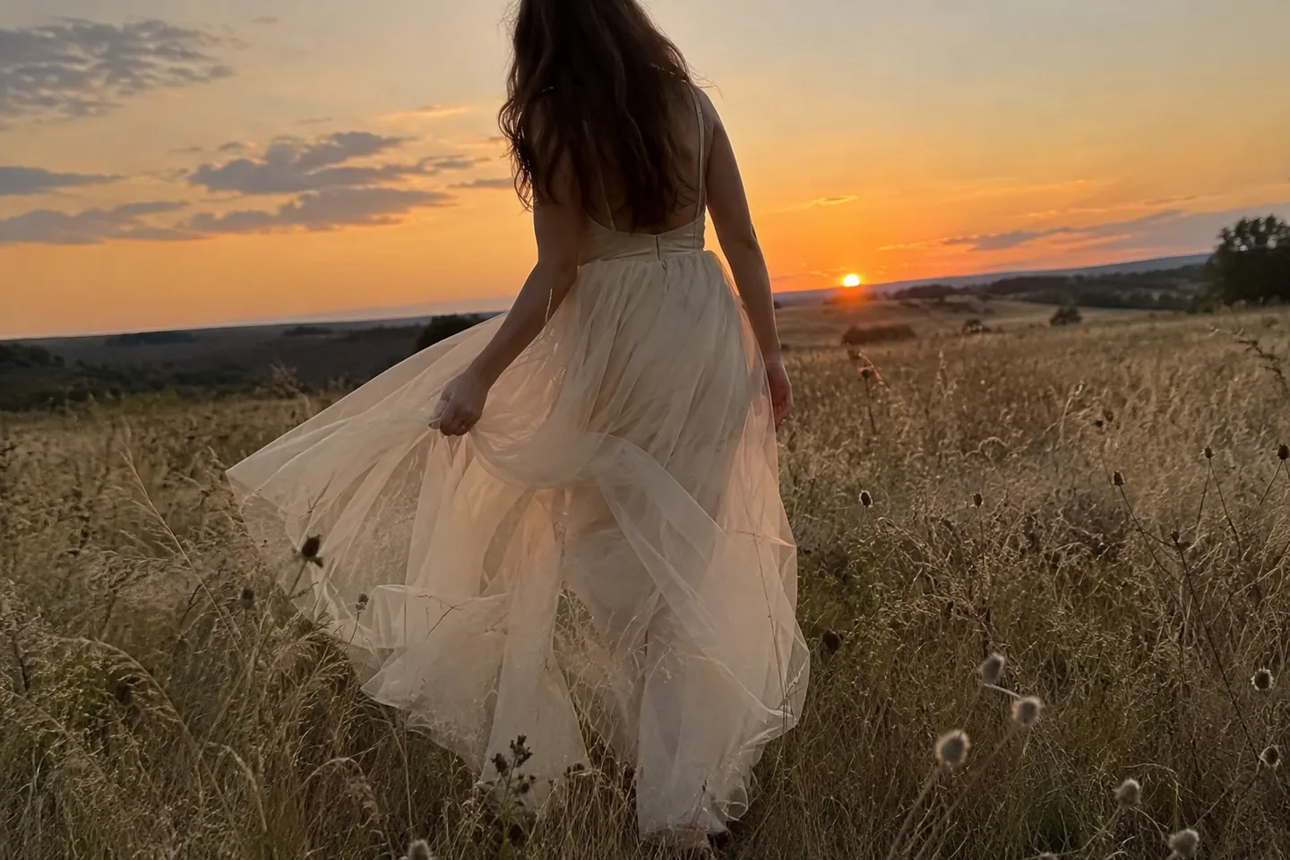 A tulle skirt lifting in the breeze as a woman walks through tall grass at sunset
