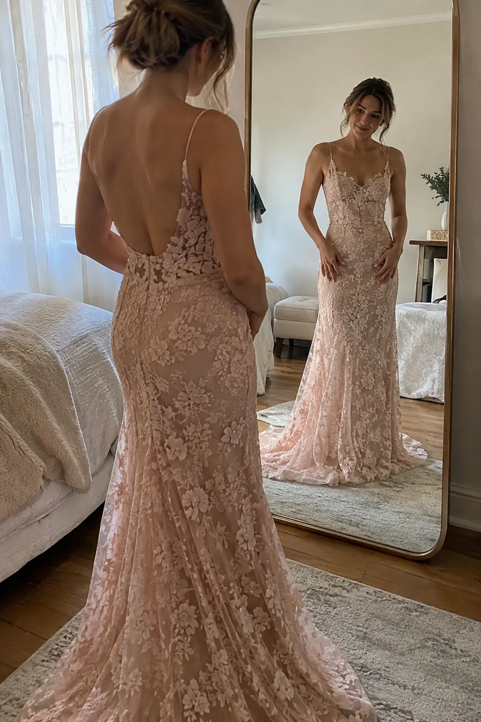 An adult woman in a blush lace gown checking the fit in a full-length mirror