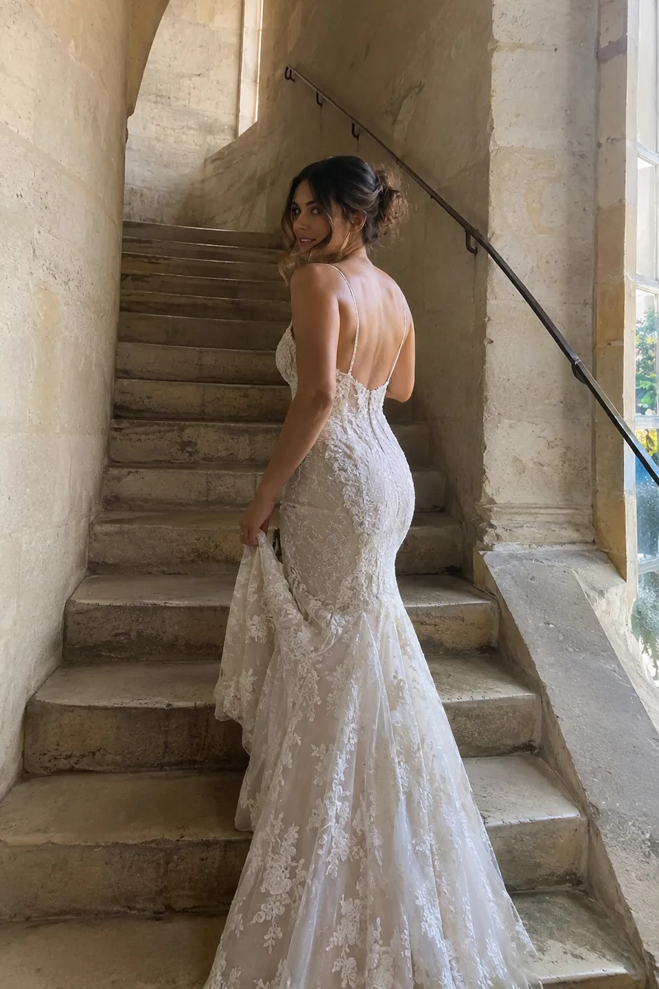 A woman in a lace mermaid gown looking back over her shoulder on a stone staircase